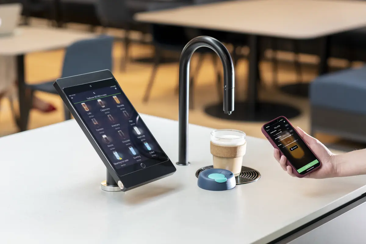 Image showing a matte black TopBrewer coffee machine with a reusable coffee cup under the swan neck and the TopBrewer app on an iPhone