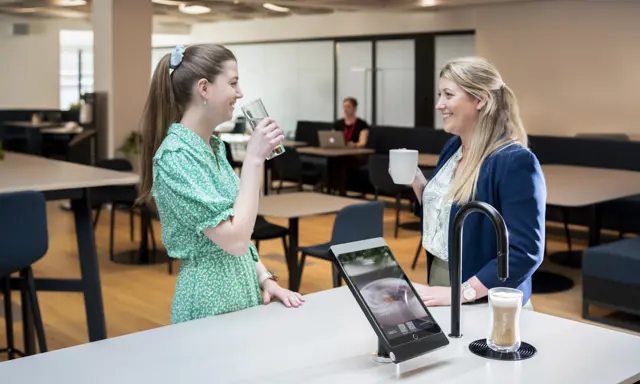 Image showing two people chatting next to a matte black TopBrewer with deluxe iPad holder