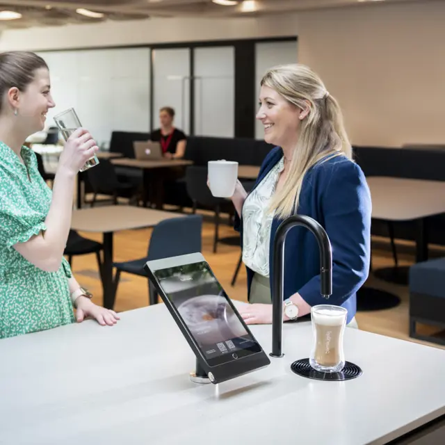 Image showing two people chatting next to a matte black TopBrewer with deluxe iPad holder