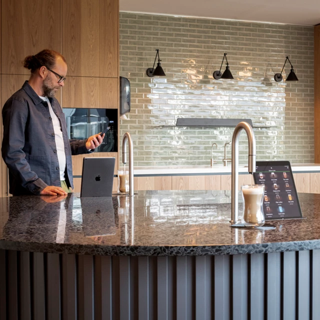 2 TopBrewer coffee machines built into a circular island, with a man in the background looking at his phone
