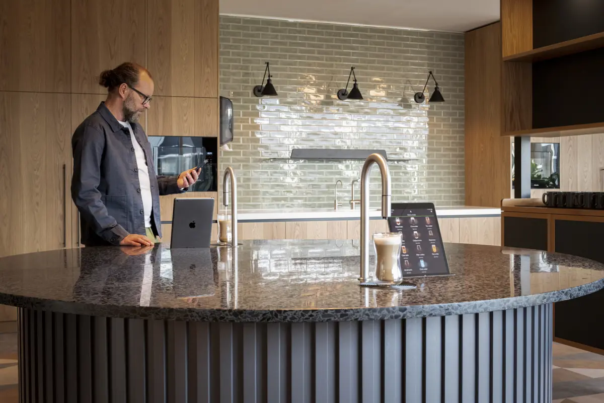 2 TopBrewer coffee machines built into a circular island, with a man in the background looking at his phone