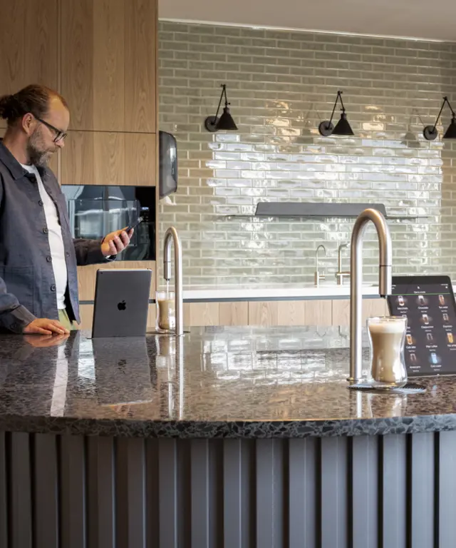 2 TopBrewer coffee machines built into a circular island, with a man in the background looking at his phone
